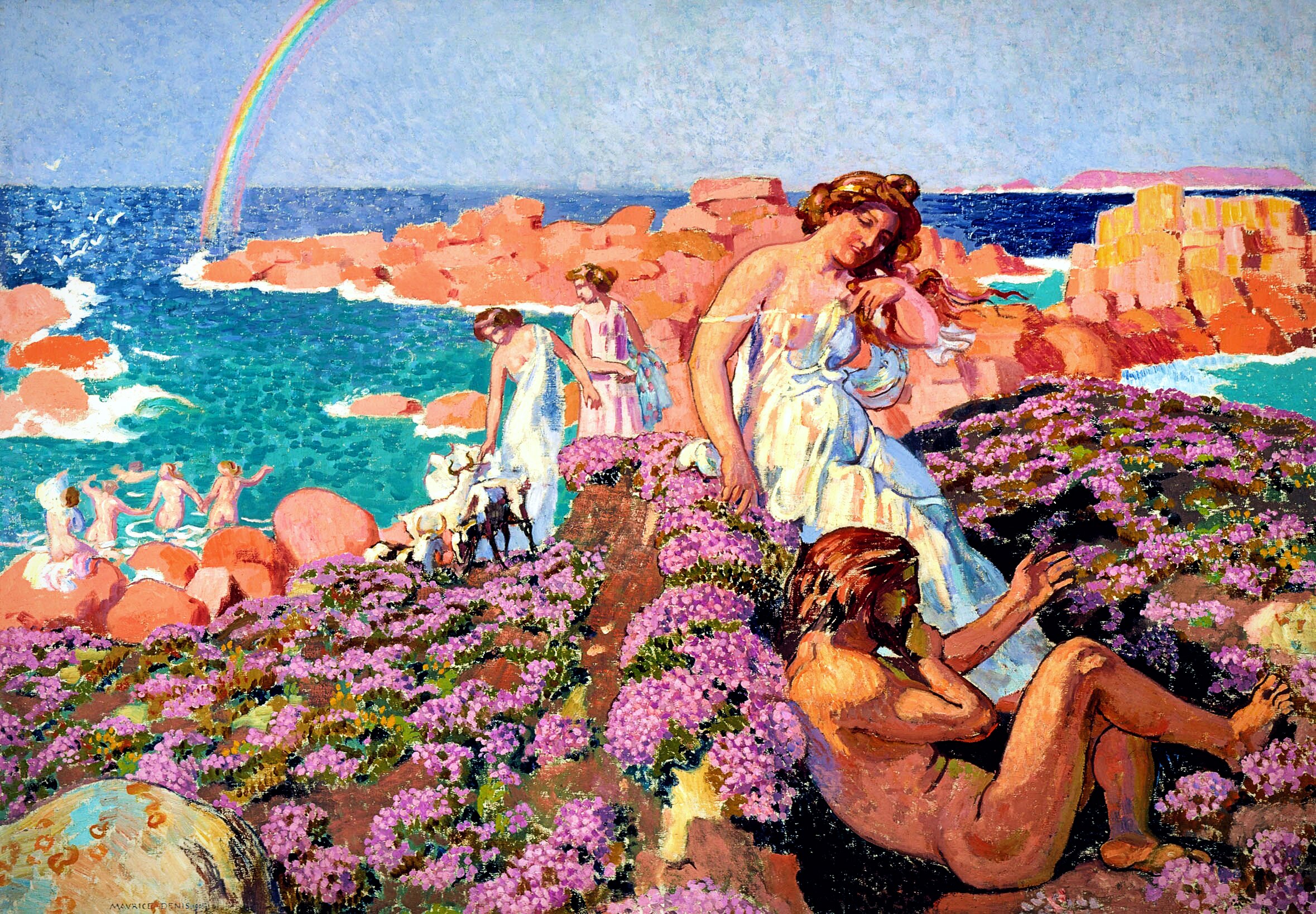 Painting depicting a sun-drenched coastal scene in a classical mythological style. In the foreground, purple wildflowers carpet rocky terrain where a reclining nude male figure reclines while a draped woman in white and blue leans toward him. Behind them, two robed women tend to goats near the water's edge. In the background, several nude figures wade and play among pink-orange boulders along a vivid turquoise sea. A rainbow arcs across a pale blue sky in the upper left. The palette is warm and saturated. Coral rock, lavender bloom, aqua water.