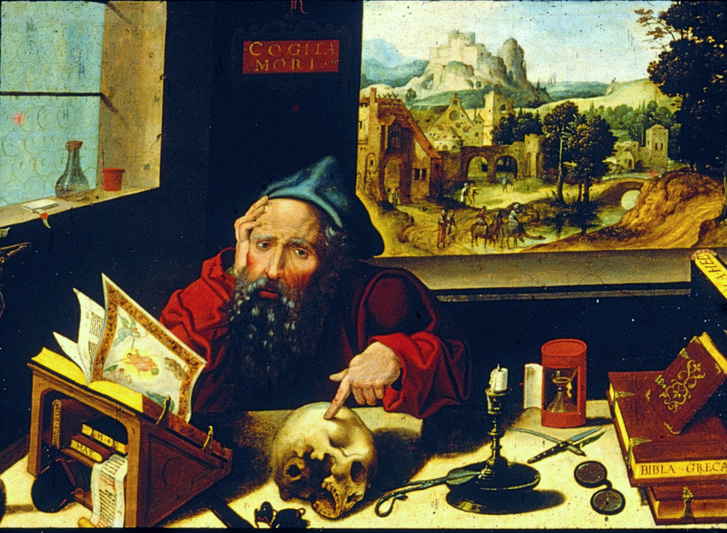Northern Renaissance oil painting of an elderly bearded scholar in a red robe and blue cap, seated at a cluttered desk, resting his head on one hand while pointing at a human skull with the other. The desk holds an open illuminated manuscript, a book labeled 'Biblia Greca,' a Hebrew scroll, an hourglass, a candle, spectacles, and a penknife. A red plaque above reads 'COGITA MORI' (contemplate death). Through an open window behind him, a landscape unfolds with a hilltop castle, a village, and small figures on a road.