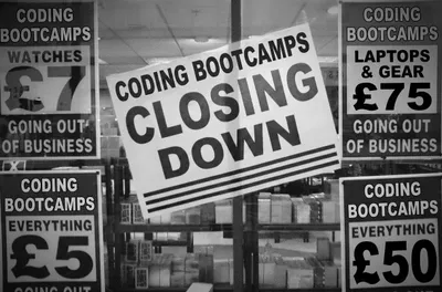 Black and white photograph of a store window displaying a large 'CODING BOOTCAMPS CLOSING DOWN' sign. Surrounding signs advertise clearance sales including 'WATCHES £7', 'LAPTOPS & GEAR £75', 'EVERYTHING £5', and 'EVERYTHING £50', all marked as 'GOING OUT OF BUSINESS'.