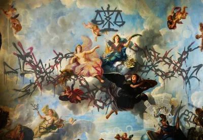 A Baroque-style allegorical ceiling painting depicting classical female figures representing virtues or goddesses, including one crowned figure in pink robes and one in blue holding a quill and documents, seated on clouds surrounded by cherubs. Additional allegorical figures appear in the lower register, one holding an olive branch with a molecular diagram drawn on her chest, another carrying a shield and spear. Scattered legal documents float in the lower right corner. Overlaid across the entire composition is aggressive graffiti tagging in black and deep red, with a graffiti rendering of the scales of justice at the top center.