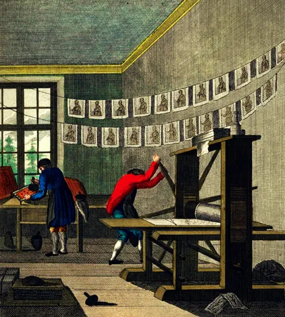 Historical engraving depicting a print shop in the 18th century. Two workers in period clothing operate a wooden printing press: one figure in a red coat pulls the press lever while bent over the press bed, and another in a blue coat inks type at a compositing table near a multi-paned window. Freshly printed sheets, each bearing a small portrait, hang in two rows on drying lines strung across the room. Ink balls, tools, and other workshop materials are scattered on the floor.