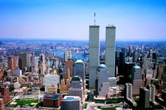 Aerial view of Lower Manhattan with the World Trade Center's Twin Towers rising above the surrounding skyline, with the East River, Brooklyn Bridge, and Manhattan Bridge visible in the background.